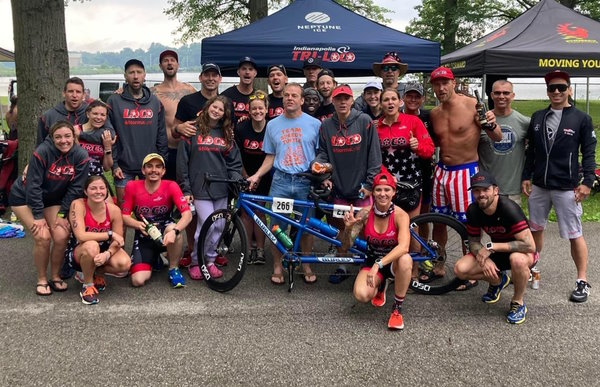 Group of 25 people posing with tandem bicycle in the forefront