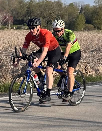 Two men on tandem bike, the rear rider drinking water